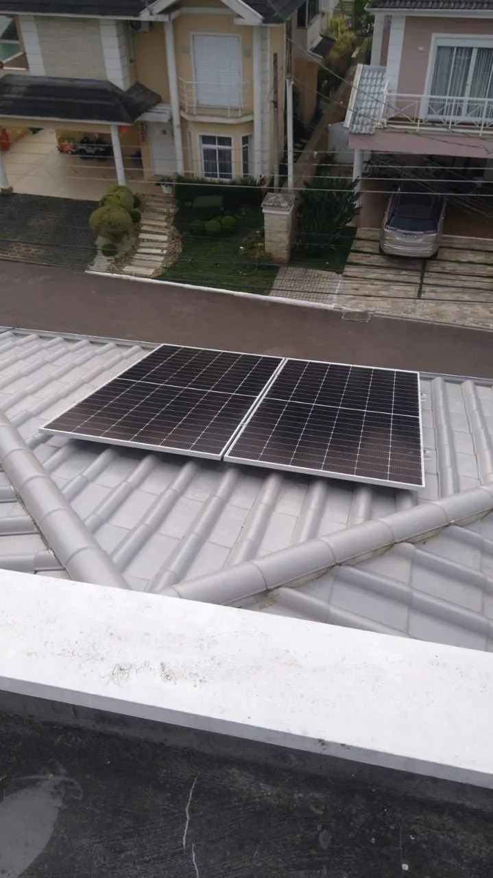 Dois módulos fotovoltaicos posicionados sobre telhado de telhas claras durante a instalação