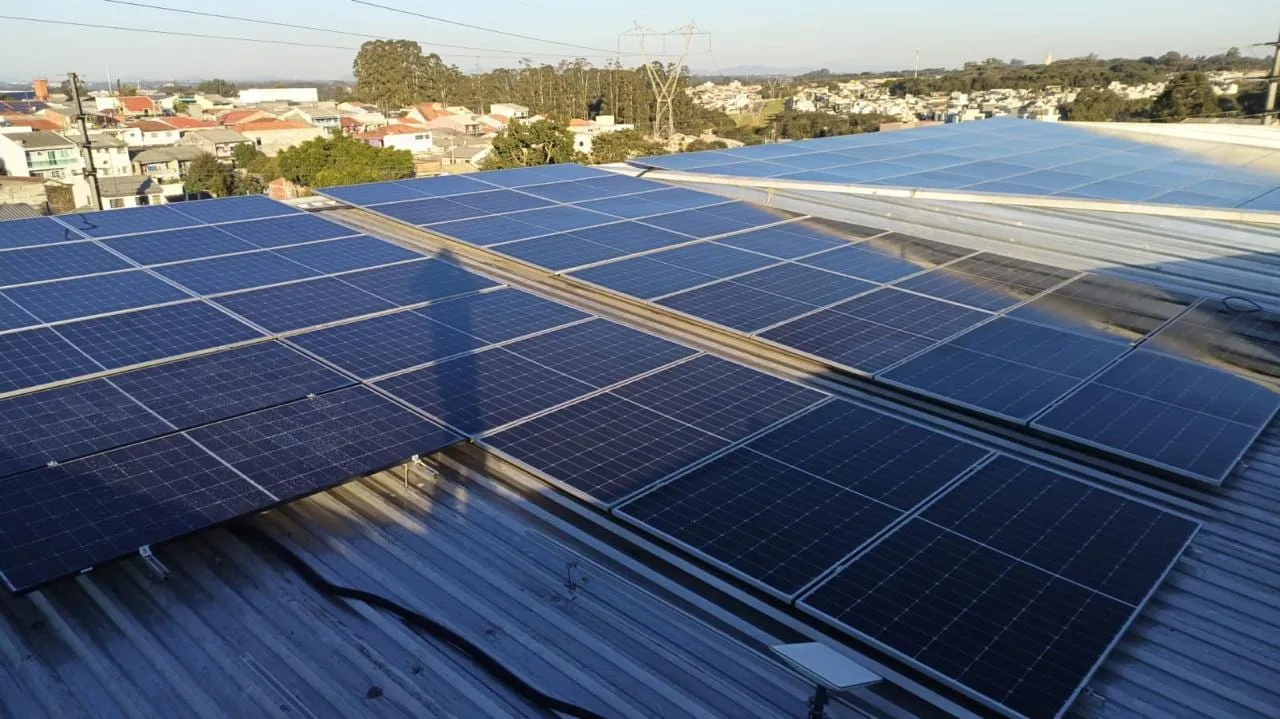 Fileiras de painéis solares em telhado metálico com a cidade ao fundo