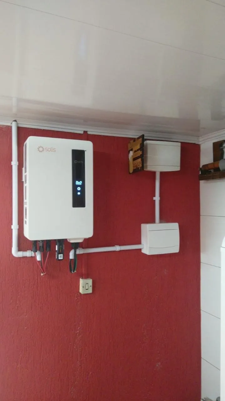 Inversor solar instalado em parede vermelha, com caixas de passagem e eletrodutos